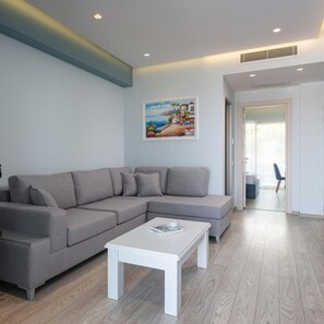 Una sala de estar con un sofá seccional gris, una mesa de centro blanca y un cuadro con una escena costera.
