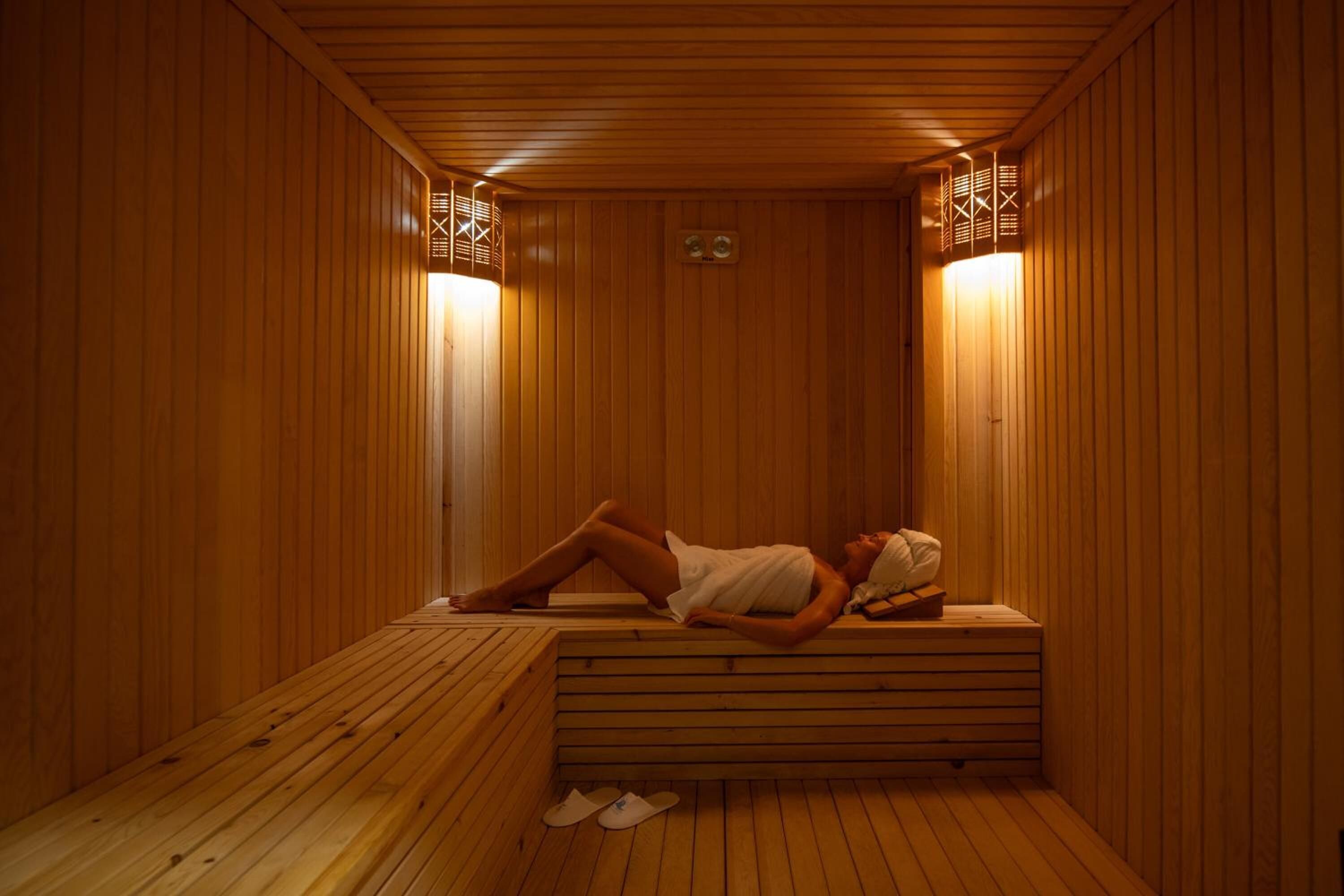 A wooden sauna with a bench and a person lying on it.
