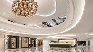 A spacious lobby with a central reception desk, a grand chandelier, and a high ceiling with skylights. - Sirin Exclusive Hotel and Residence (Pattaya)