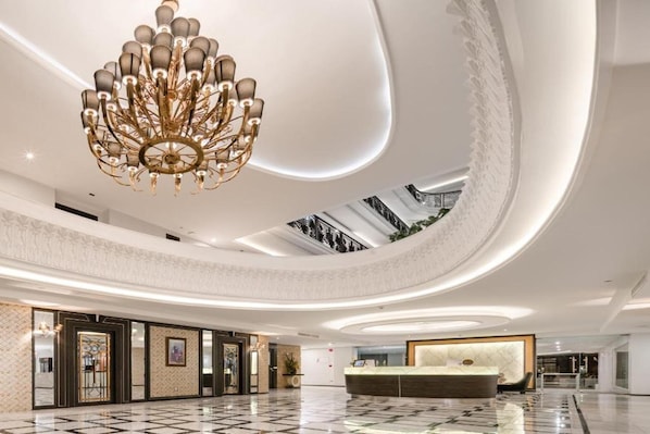 Un hall d’entrée spacieux, doté d’un comptoir d’accueil central, d’un magnifique lustre et d’un plafond haut orné de verrières.