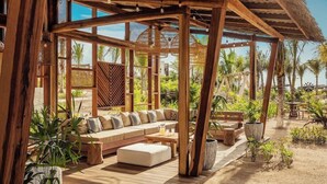 A covered outdoor seating area with a wooden bench, a sofa, and a table. - Jungala Hotel at Vidantaworld Riviera Maya (Playa del Carmen)