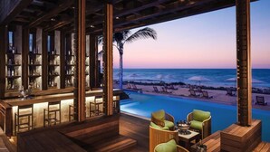 A bar area with a view of the beach and pool at dusk. - Jungala Hotel at Vidantaworld Riviera Maya (Playa del Carmen)