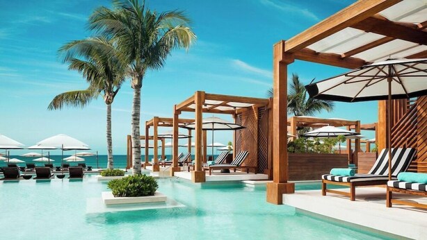 A pool area with lounge chairs and umbrellas, surrounded by wooden pergolas and palm trees. - Jungala Hotel at Vidantaworld Riviera Maya (Playa del Carmen)