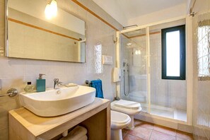 A bathroom with a large sink, toilet, and glass-enclosed shower. - Cala Fiorita (Budoni)