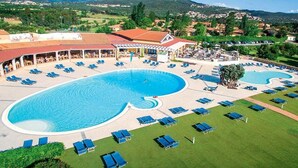 A resort with a large swimming pool, sun loungers, and a covered area with tables and chairs.