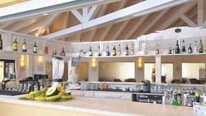 A spacious bar area with multiple shelves of liquor bottles, a central bar counter with various items, and a high ceiling with wooden beams.