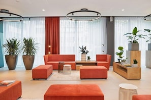 Un hall d’entrée moderne avec un ensemble de canapés rouges, de grandes plantes en pot et une console en bois.