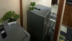 Un espacio habitable pequeño con un refrigerador, una pequeña planta en maceta, un control remoto y un televisor montado.