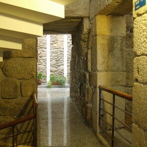 Un escalier en pierre avec une rampe métallique, menant à un mur de pierre percé d’une porte.