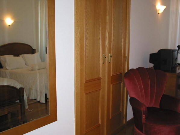 A room with a wooden wardrobe, a bed with white bedding, a red armchair, and a television. - Santos Hotel (Guarda)