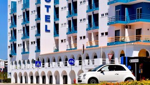 Hotelli, jonka yläpuolella on suuri, selkeästi näkyvä «HOTEL»-kyltti, siinä on useita parvekkeita ja valkoinen auto on pysäköity sen eteen.