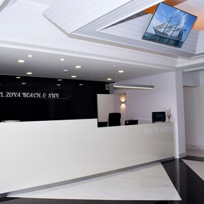 A reception desk with a 'Welcome' sign, a black wall with 'L ZOYA BEACH & SUN' text, and a ceiling with a ship image. - THE FOZ Beach Hotel (Figueira da Foz)