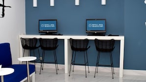 Aula, jossa on sininen seinä, kaksi näyttöä, joissa näkyy hotellin nimi, sekä valkoinen vastaanottotiski, jonka edessä on neljä mustaa tuolia.