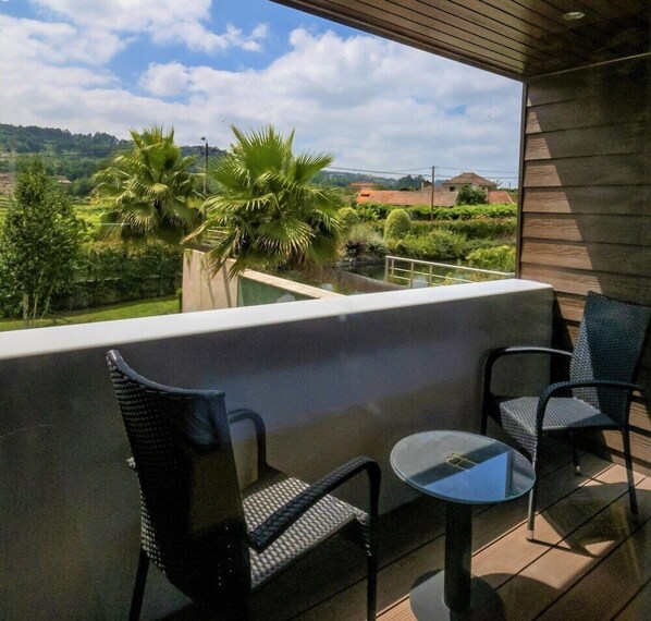 A balcony with two chairs and a small table, overlooking a lush landscape with palm trees and distant hills. - FH Hotel Rural (Felgueiras)