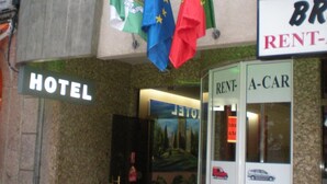 Entrada de hotel con banderas, un letrero de alquiler de coches y un anuncio que indica un restaurante.