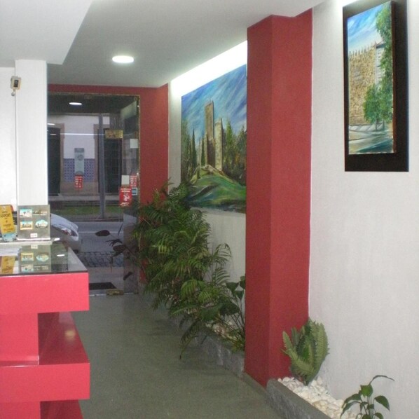 A reception area with a red counter, a painting of a castle, and a view of a building through a glass door. - Hotel Dom Joao IV (Guimarães)