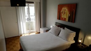 Habitación de hotel con una cama grande, un televisor de pantalla plana en la pared, una puerta corrediza de vidrio que da a un balcón y un cuadro sobre la cama.