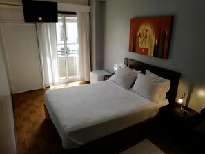 A hotel room with a large bed, a flat-screen TV mounted on the wall, a sliding glass door leading to a balcony, and a painting above the bed. - Hotel Dom Joao IV (Guimarães)