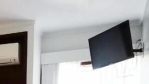 Habitación de hotel con cama, televisor de pantalla plana montado en la pared y ventana con cortinas.