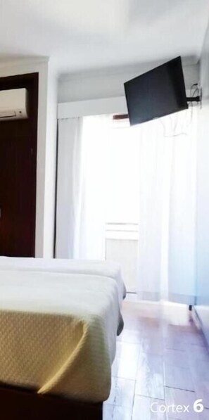 A hotel room with a bed, a flat-screen TV mounted on the wall, and a window with curtains. - Hotel Dom Joao IV (Guimarães)