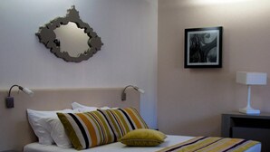 A hotel room with a bed, pillows, a bedside table with a lamp, a wall-mounted mirror, and a framed picture. - Paredes Design Hotel (Paredes)