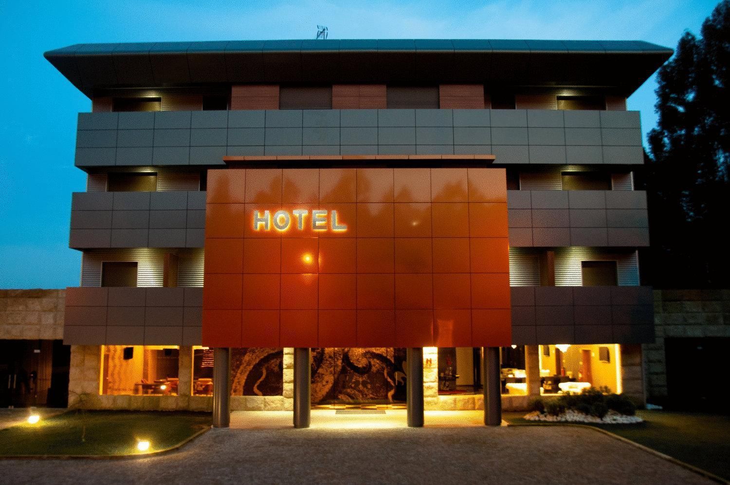 Un hotel moderno con un llamativo letrero que dice 'HOTEL', varios pisos y una entrada bien iluminada.