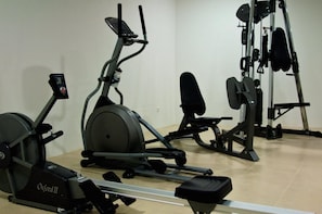 A gym with an elliptical, a bench, and a weight machine. - Paredes Design Hotel (Paredes)