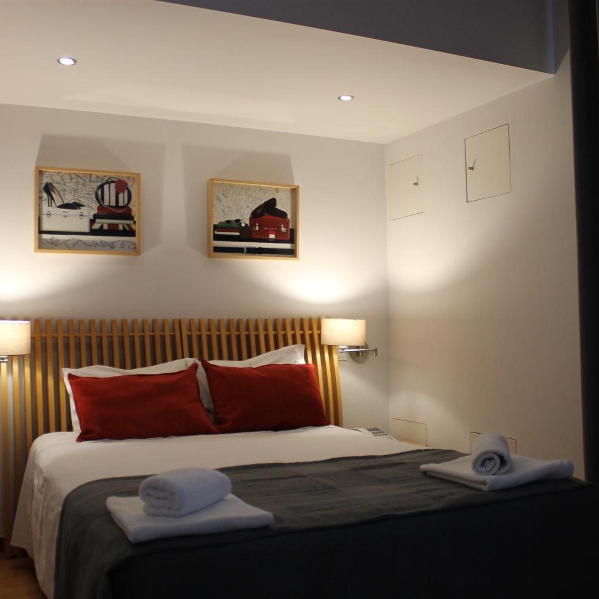 Una habitación de hotel con una cama, dos lámparas de pared y dos cuadros enmarcados sobre la cama.