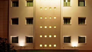 Un edificio de hotel con varios pisos, un letrero llamativo que dice 'HOTEL PAULO VI' y un estacionamiento con coches.