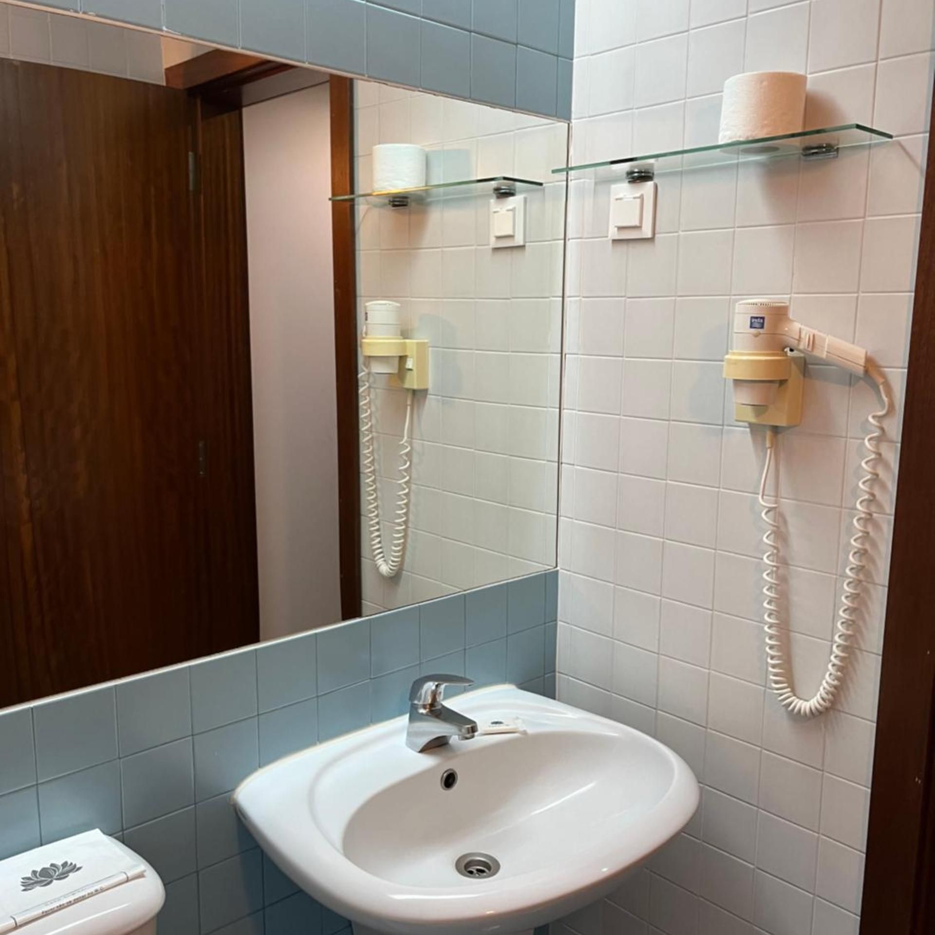 Un baño con un lavamanos blanco, un espejo y dos secadores de pelo fijados en la pared.