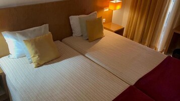 Una habitación de hotel con una cama, almohadas, una mesita de noche y una lámpara.