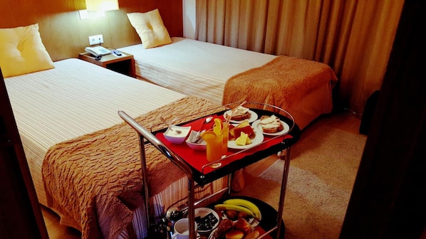 A hotel room with two beds, a small table with breakfast items, and a suitcase on the floor. - Hotel Jose Alberto (Viseu)