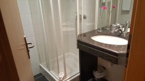 Een badkamer met een glazen douchecabine, een wastafel met een granieten blad en een spiegel met bloemdecoratie.