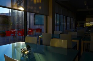 Un comedor moderno con mesas y sillas de vidrio, ventanas amplias y vistas al exterior.