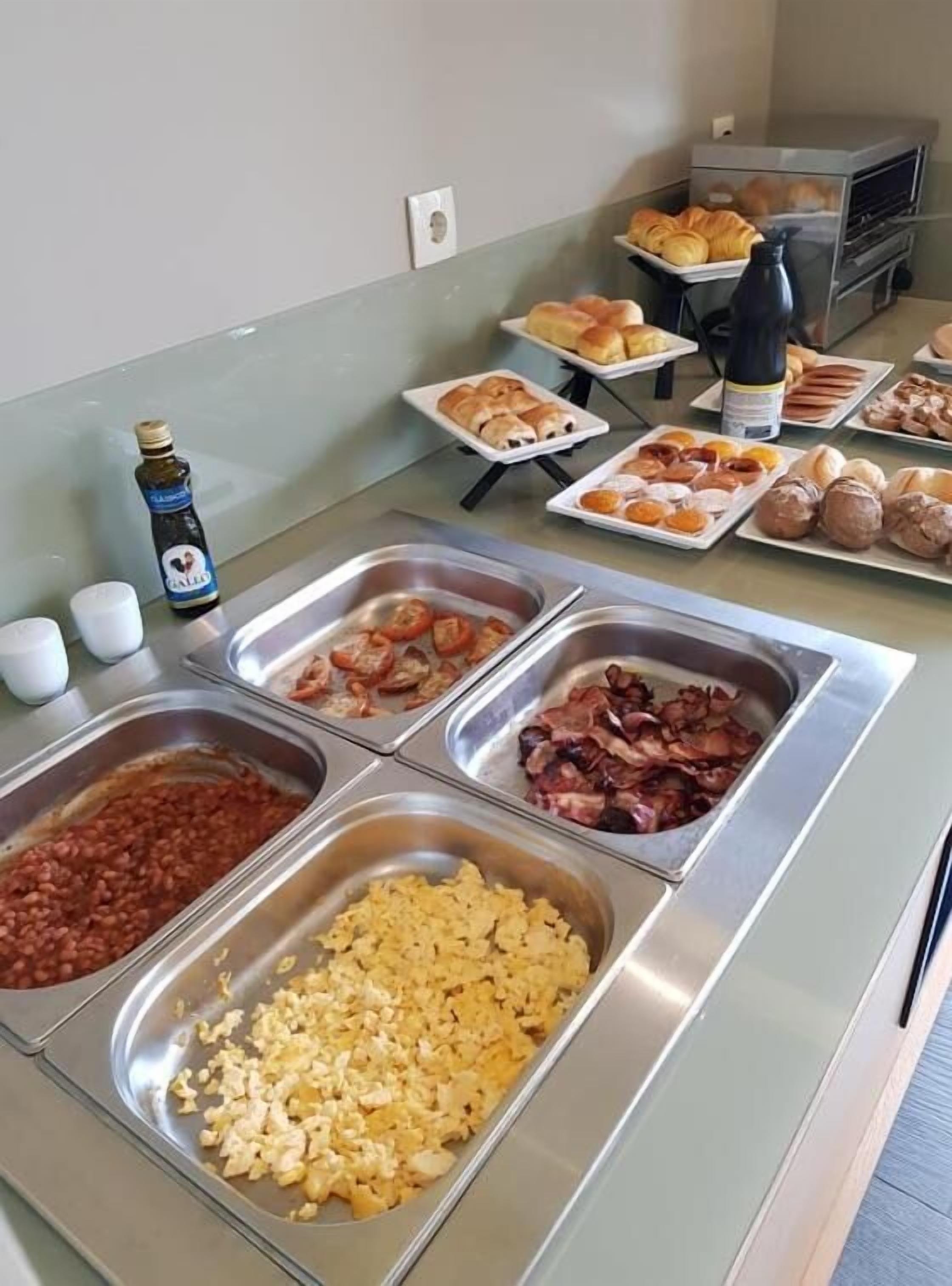A buffet with various food options including beans, scrambled eggs, bacon, and pastries.