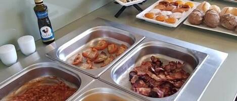 A buffet with various food options including beans, scrambled eggs, bacon, and pastries.
