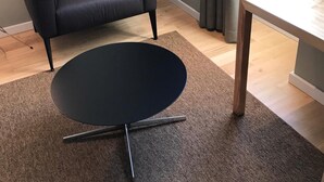 A room with a black leather chair, a small black table, a wooden floor, and a grey wall. - Penedono Medieval Hotel (Penedono)