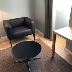 A room with a black leather chair, a small black table, a wooden floor, and a grey wall. - Penedono Medieval Hotel (Penedono)