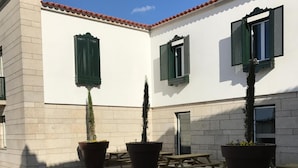 A courtyard with potted plants, wooden benches, and a building with white walls and green shutters. - Penedono Medieval Hotel (Penedono)