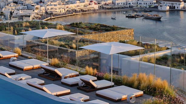 A coastal resort with a swimming pool, sun loungers, and a view of a white-washed town by the sea. - Deos Mykonos (Mykonos)