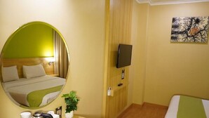 A hotel room with a bed, a bedside table with a kettle, a mirror, a television, and a painting on the wall. - Syariah Hotel Sentul (Bogor)