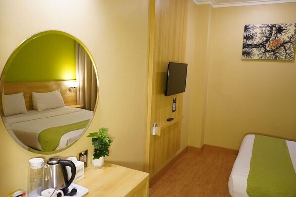 Ein Hotelzimmer mit einem Bett, einem Nachttisch mit Wasserkocher, einem Spiegel, einem Fernseher und einem Bild an der Wand.