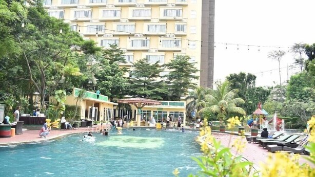 A swimming pool area with lounge chairs and a building in the background. - Syariah Hotel Sentul (Bogor)