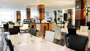 A modern dining area with white tables, black chairs, and a central counter with a coffee machine.