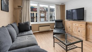 Ein modernes Wohnzimmer mit einer Couch, einem Glastisch, einem Fernseher und Blick auf Gebäude.