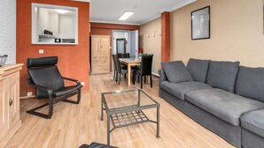 Ein Wohnzimmer mit grauem Sofa, einem schwarzen Ledersessel, einem Glastisch und einer Holzkabine.