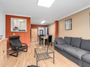 A living room with a grey sofa, a black leather chair, a glass coffee table, and a wooden cabinet. - Cosy apartment near the casino (Blankenberge)