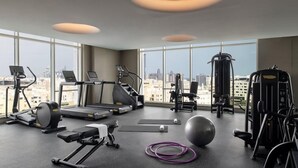 Un gimnasio moderno con máquinas de cardio, pesas y balones de ejercicio, con amplias ventanas y vista a la ciudad.