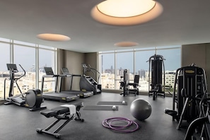 A modern gym with cardio machines, free weights, and exercise balls, featuring large windows and a city view. - Abesq Doha Hotel & Residences (Doha)