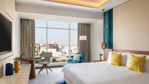 Habitación de hotel con una cama grande, un escritorio, una silla y vistas a la ciudad.